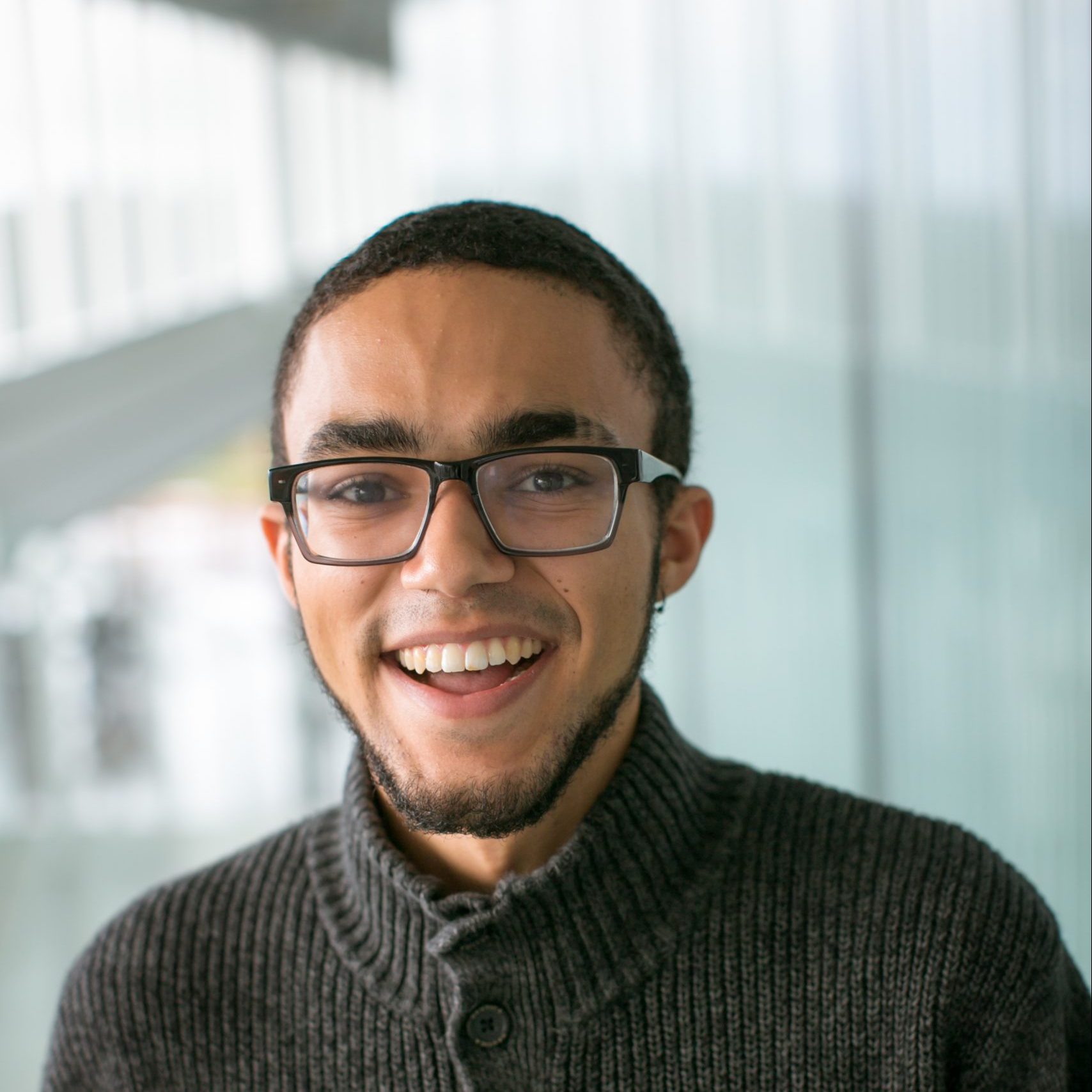 Indoor portrait of DeShae Dillard facing the camera in front of a bright, blurred hallway or windowed background.